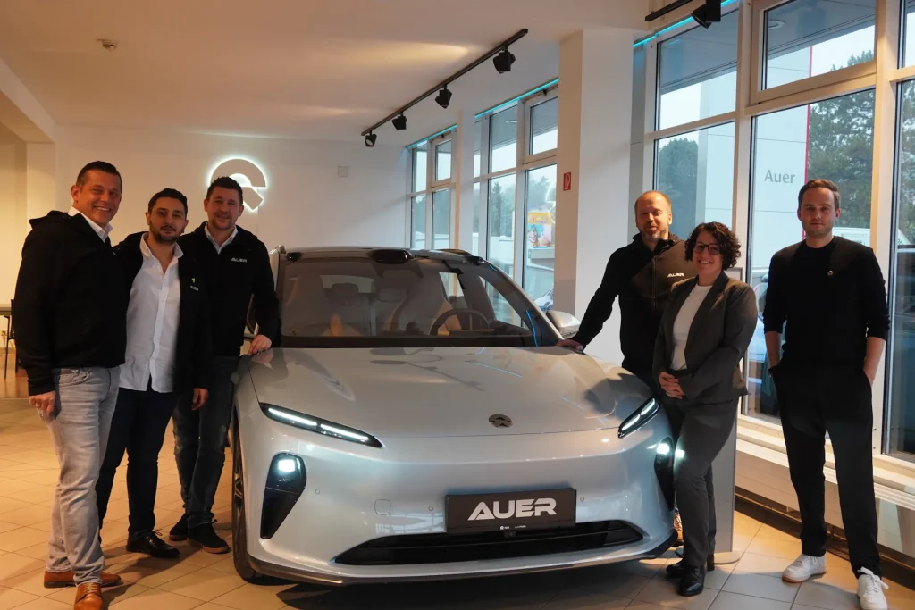 Team von Autohaus Auer steht neben einem silbernen Nio im Schauraum. Freundliche Stimmung, modernes Auto für Verkauf präsentiert.